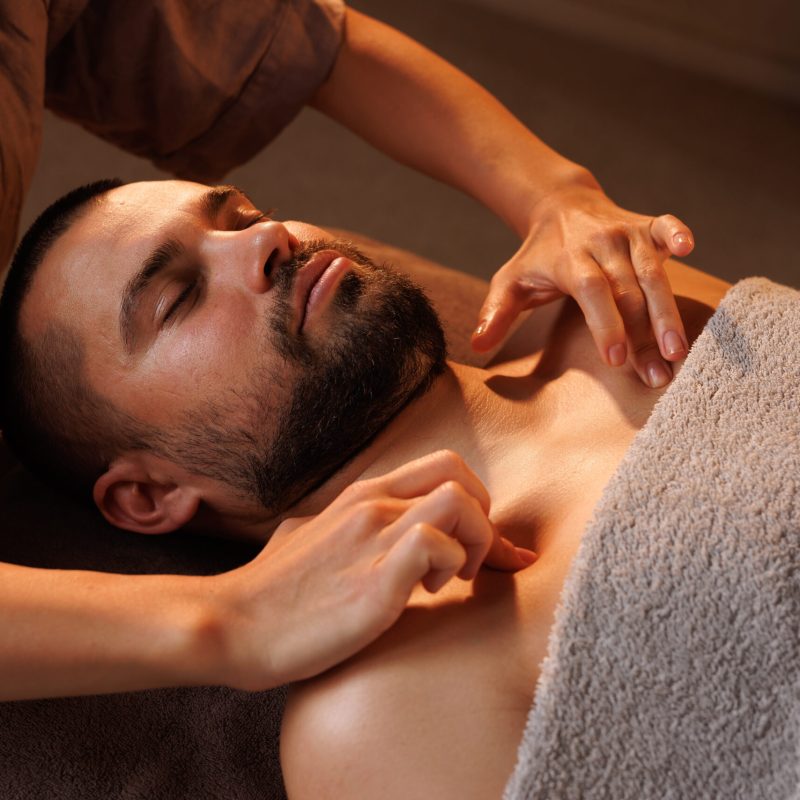 Man gets chest massage in spa, enjoying relaxing atmosphere, recovering from work. Masseuse performs therapeutic massage, restoring health.